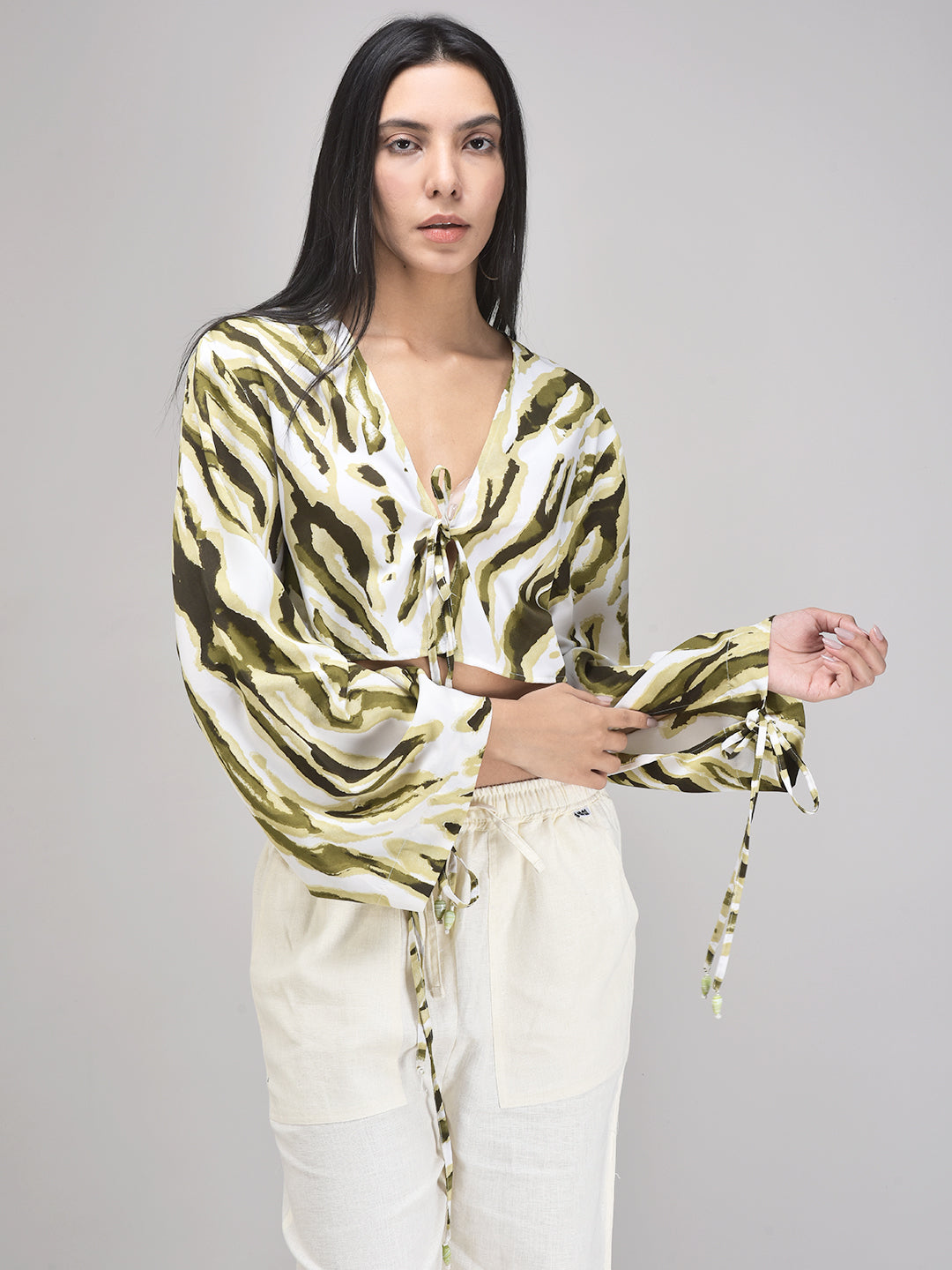 Model wearing an olive and light green abstract patterned knotted top with long sleeves and beaded details.