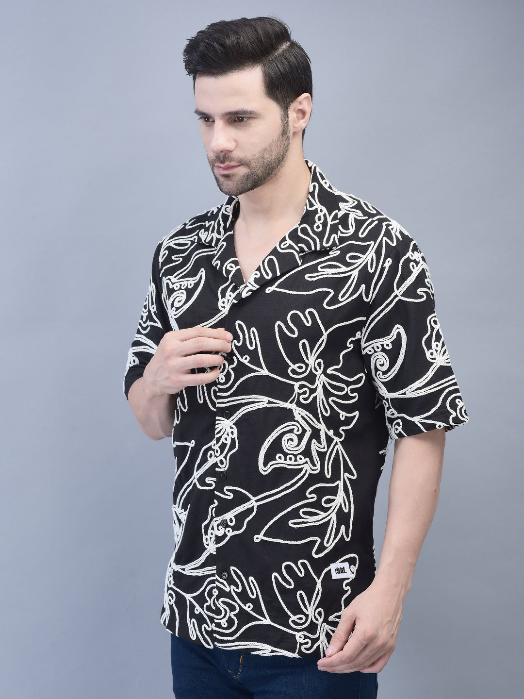 Three-quarter front view – man adjusting collar of black shirt with white embroidery