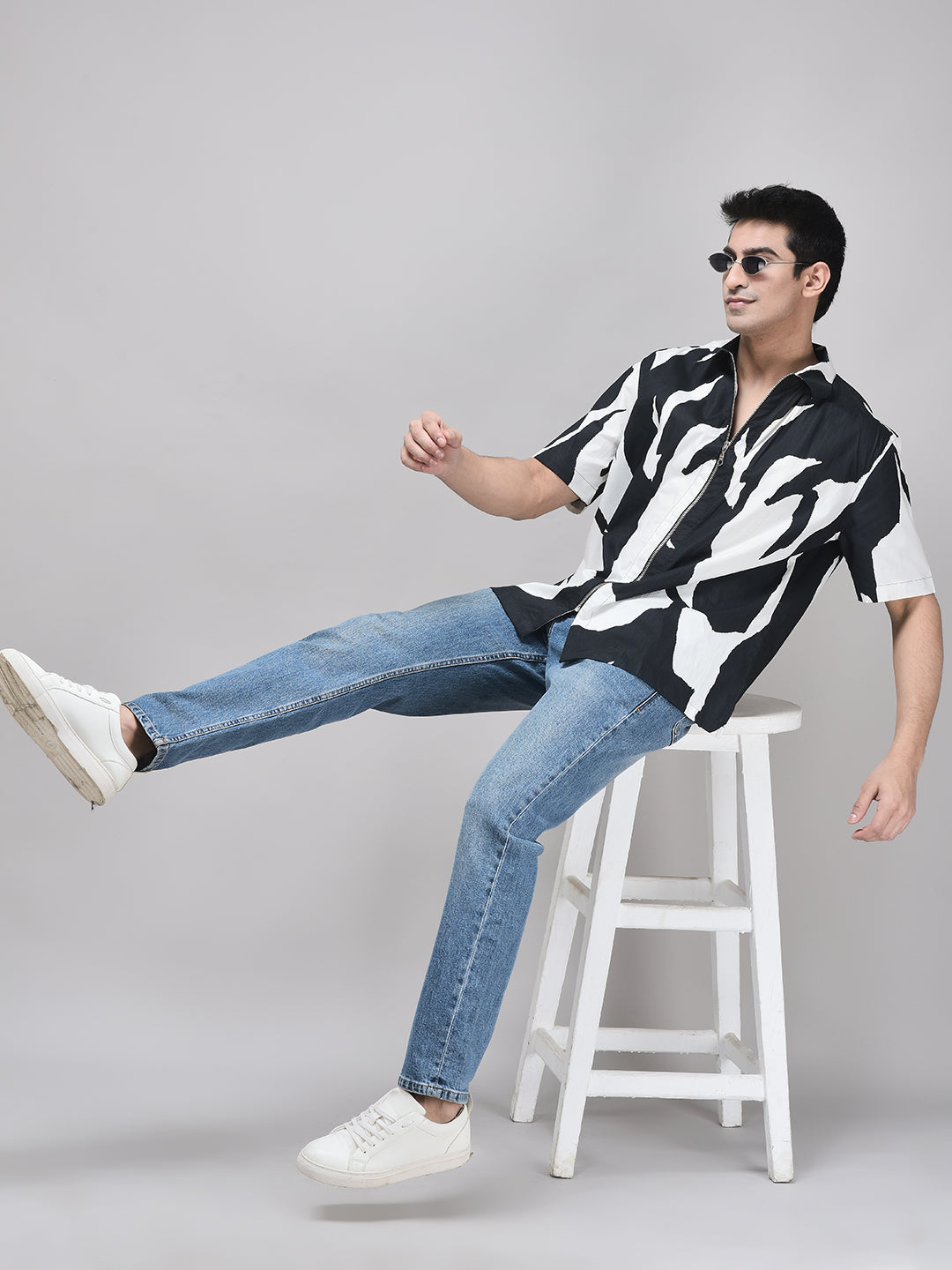 Man sitting on white stool wearing FURY shirt with black trousers – playful pose