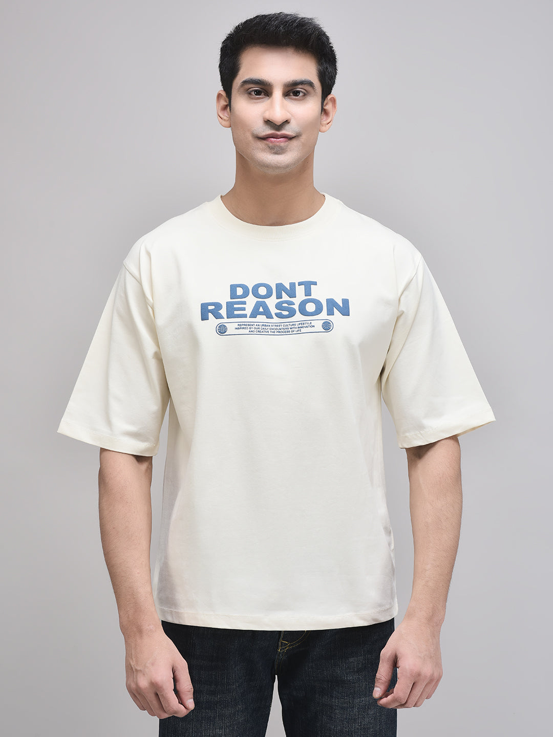 A male model wearing a beige oversized t-shirt with the text 'DON'T REASON' printed in bold letters on the front.