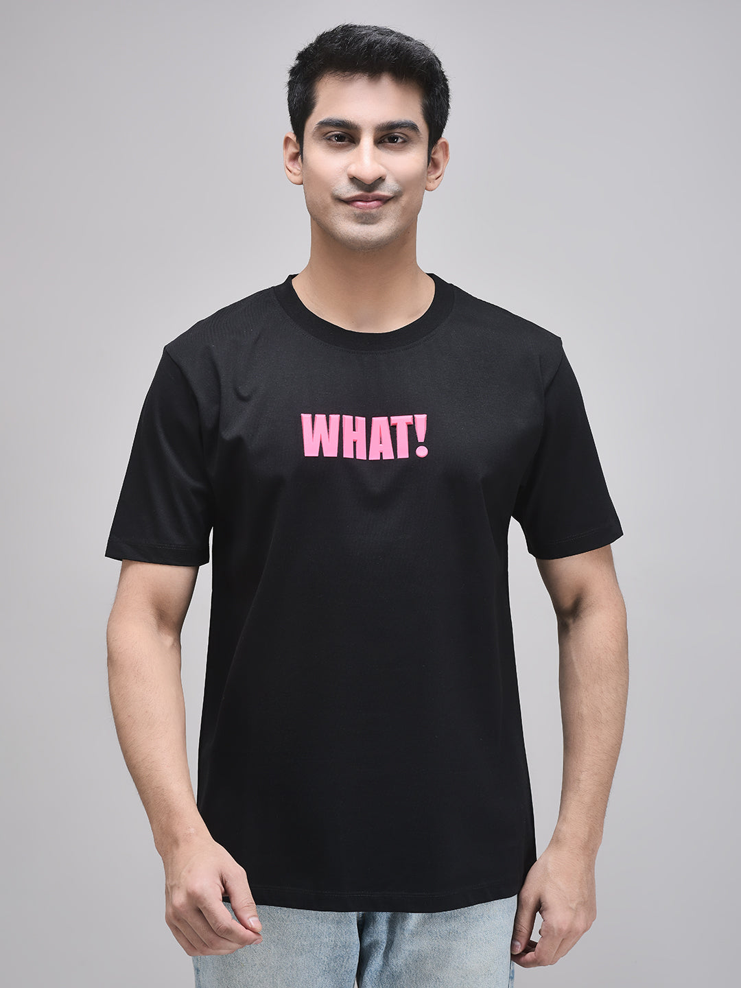 A person wearing a black crew neck t-shirt with the text 'WHAT!' printed in pink on the chest.