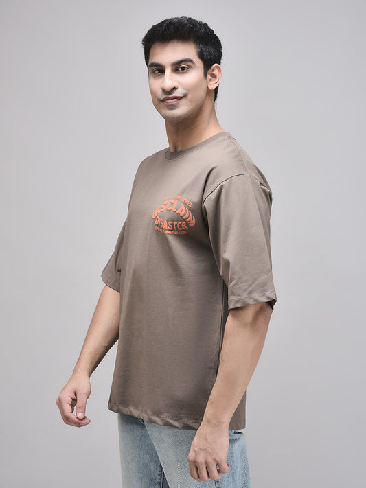 A male model wearing a gray oversized t-shirt with a graphic print in the center, paired with light blue jeans.