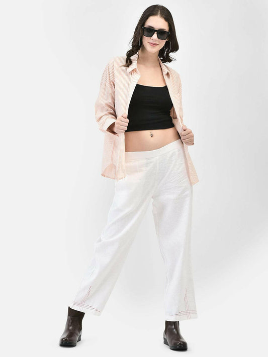 A woman modeling an oversized, long-sleeved, apricot-colored seersucker shirt with dropped shoulders, paired with white trousers and sunglasses.