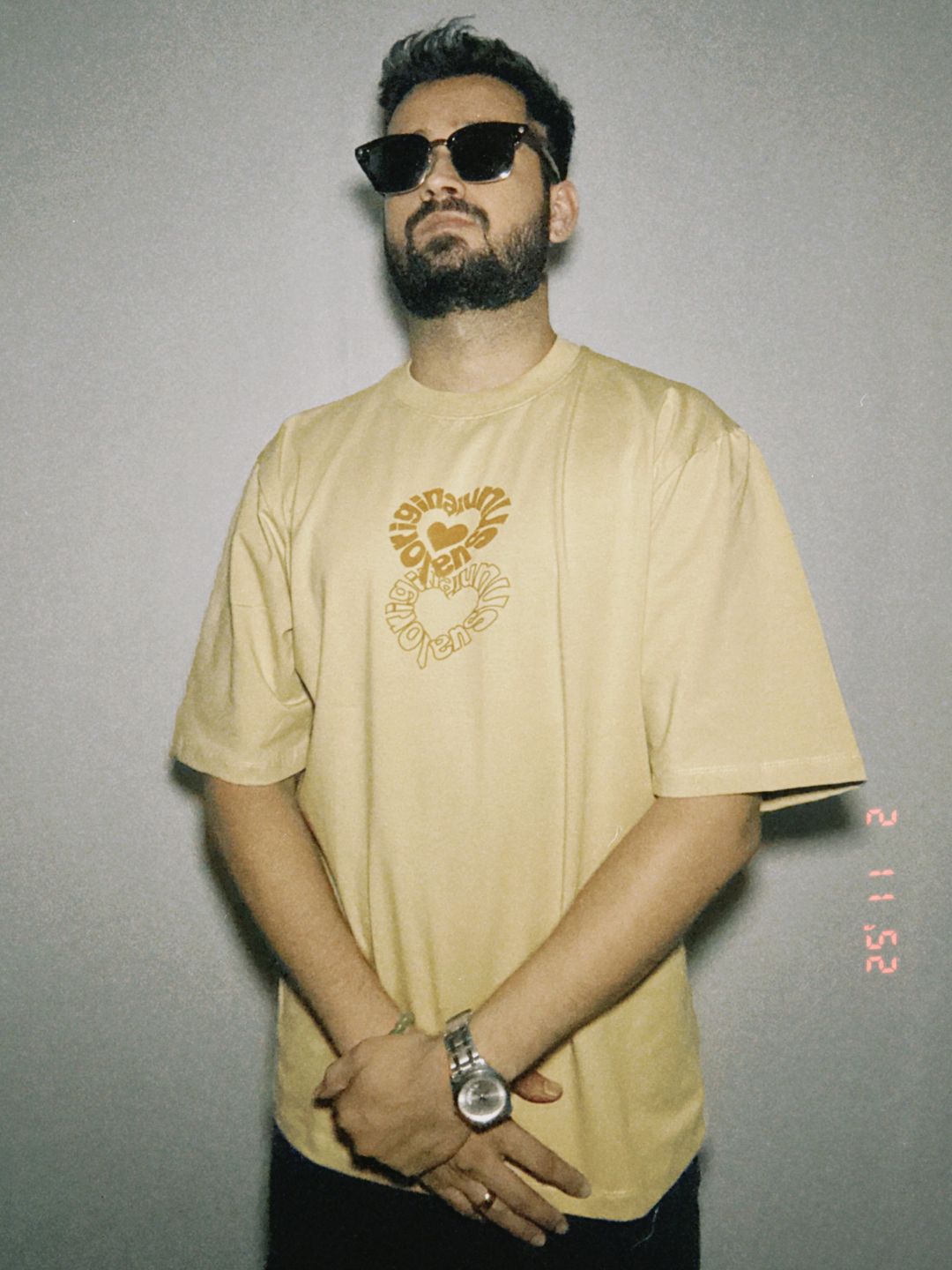 A person wearing a beige oversized t-shirt with a graphic print in the center, featuring a relaxed fit.