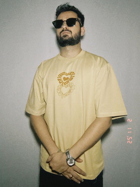 A person wearing a beige oversized t-shirt with a graphic print in the center, featuring a relaxed fit.