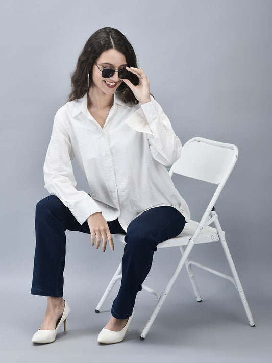 A woman sitting on a white chair wearing a white shirt with textured stripes and sunglasses.