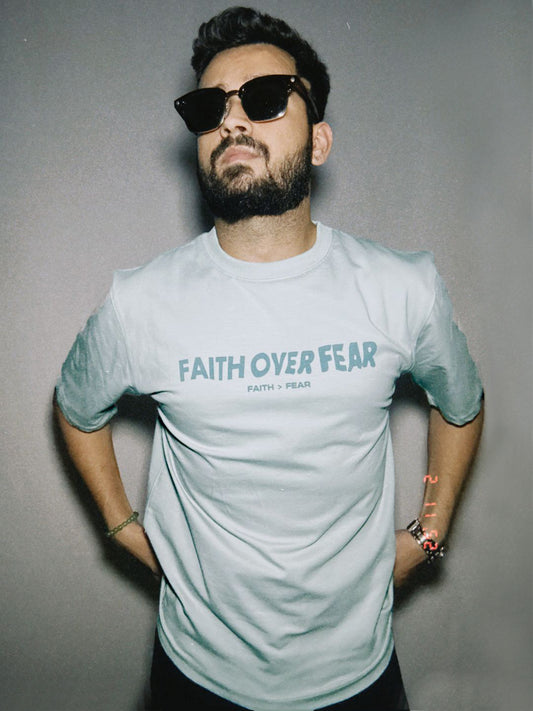 A person wearing a powder blue oversized t-shirt with the text 'FAITH OVER FEAR' printed on the front.