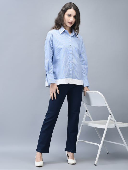 A woman standing next to a white chair, wearing a blue cotton shirt with full sleeves and a relaxed fit, designed for casual wear.