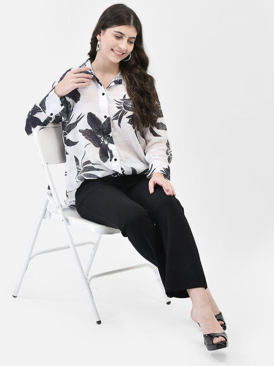 Front view of model sitting on chair in Noir Petals cotton floral shirt
