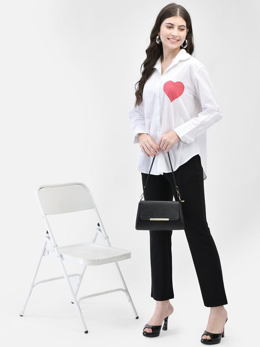 Model standing beside a white chair in white textured shirt with red heart detail and black pant