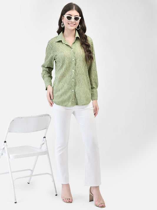 Full view of the pistachio crochet shirt styled with white trousers, woman standing near a white chair