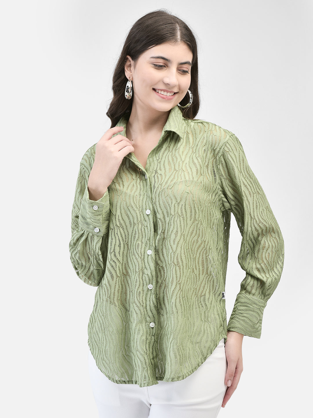 Woman wearing pistachio green crochet textured shirt with white pants, smiling and posing against a white background