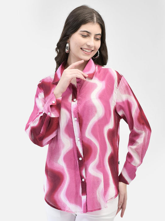 A woman smiling and posing in a pink and white checkered shirt with long sleeves.