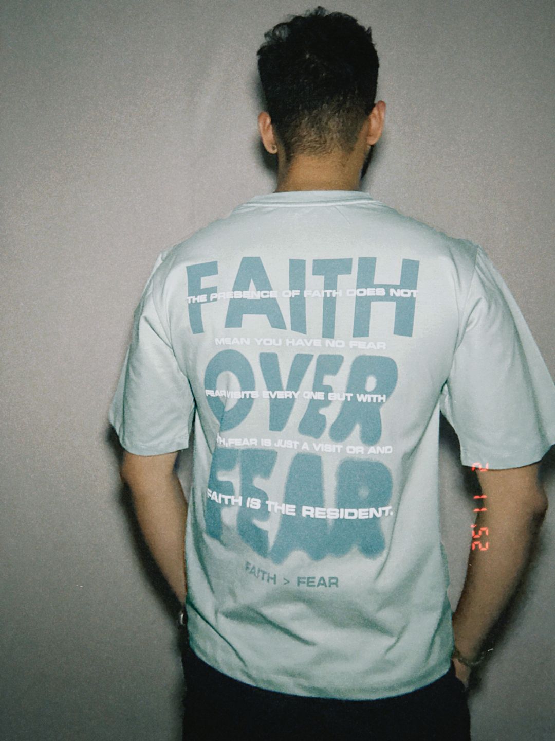 Person wearing a light blue t-shirt with text on the back against a plain background