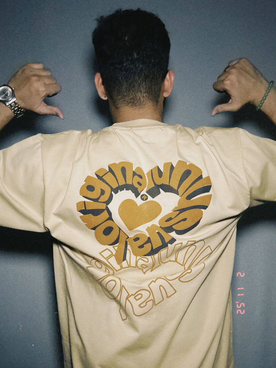 Person wearing a beige shirt with graphic design on the back against a plain background.