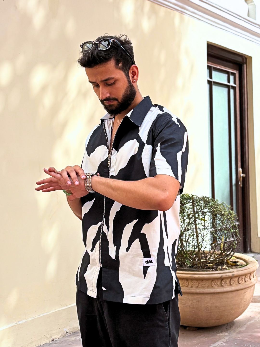 A man wearing a black and white animal patterned oversized cotton shirt with a zippered closure, paired with dark pants.
