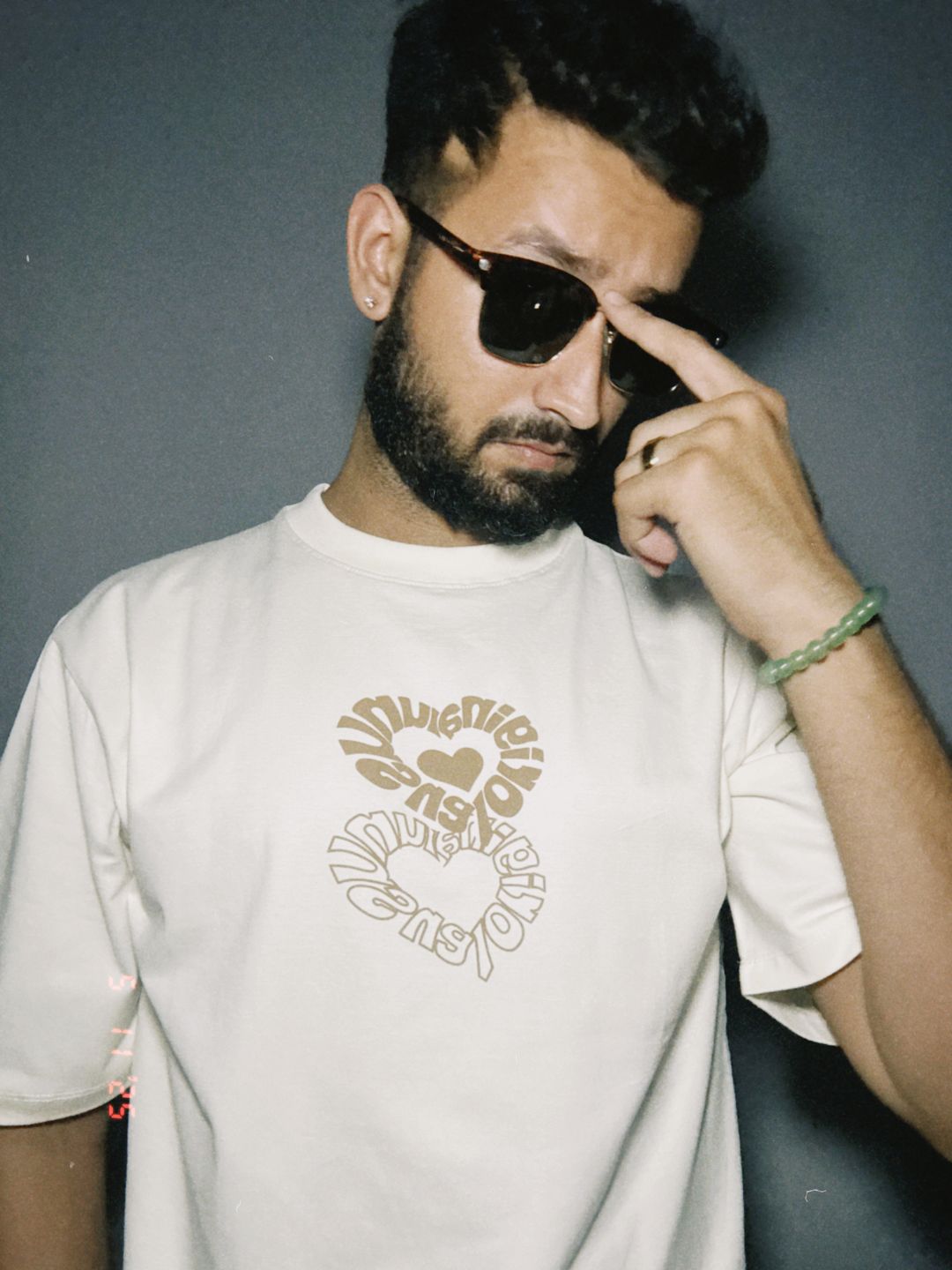 Person wearing a white t-shirt with a graphic design, holding sunglasses and pointing to their head.