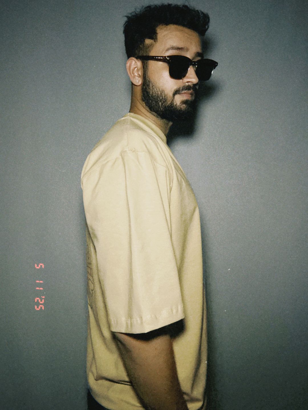 Person wearing sunglasses and a beige shirt against a dark background