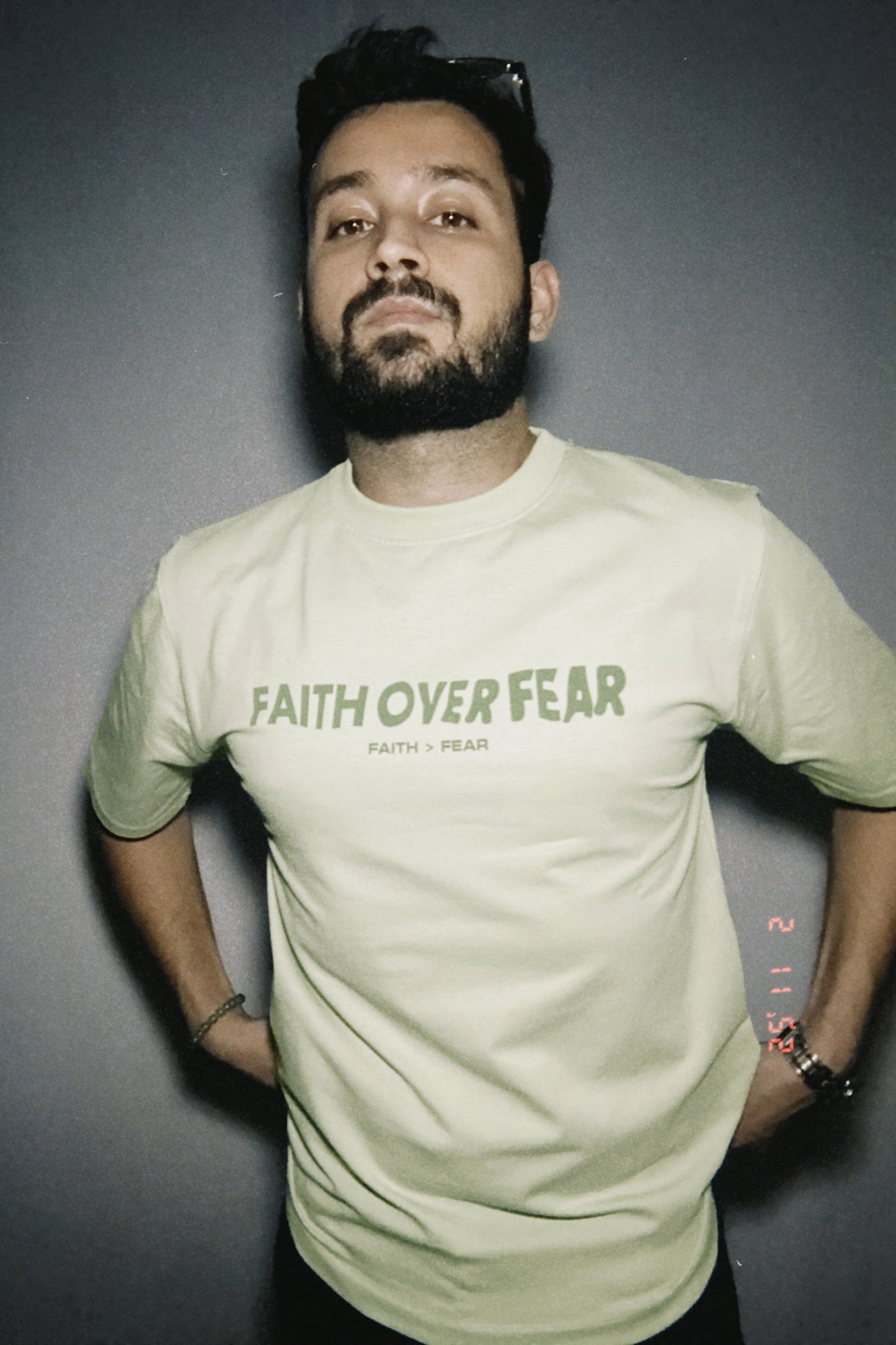 A person wearing a pastel green t-shirt with the text 'FAITH OVER FEAR' printed on the front.