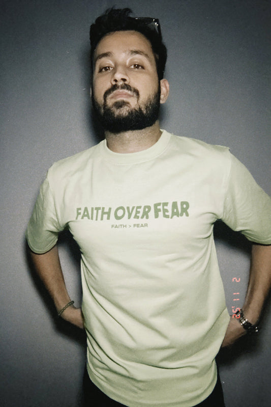 A person wearing a pastel green t-shirt with the text 'FAITH OVER FEAR' printed on the front.
