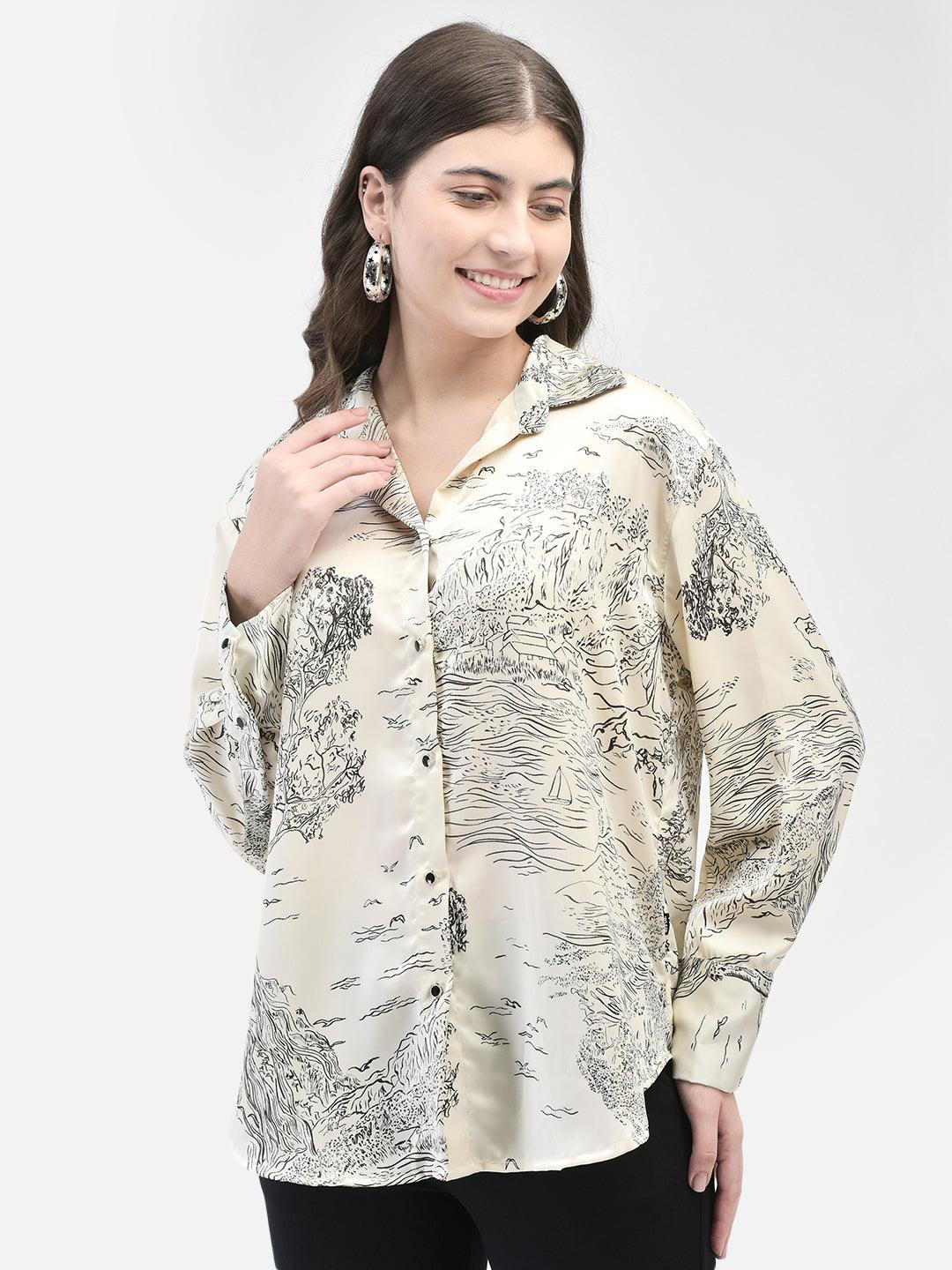 Side angle view of woman wearing beige satin shirt with abstract print, smiling with hand near collar