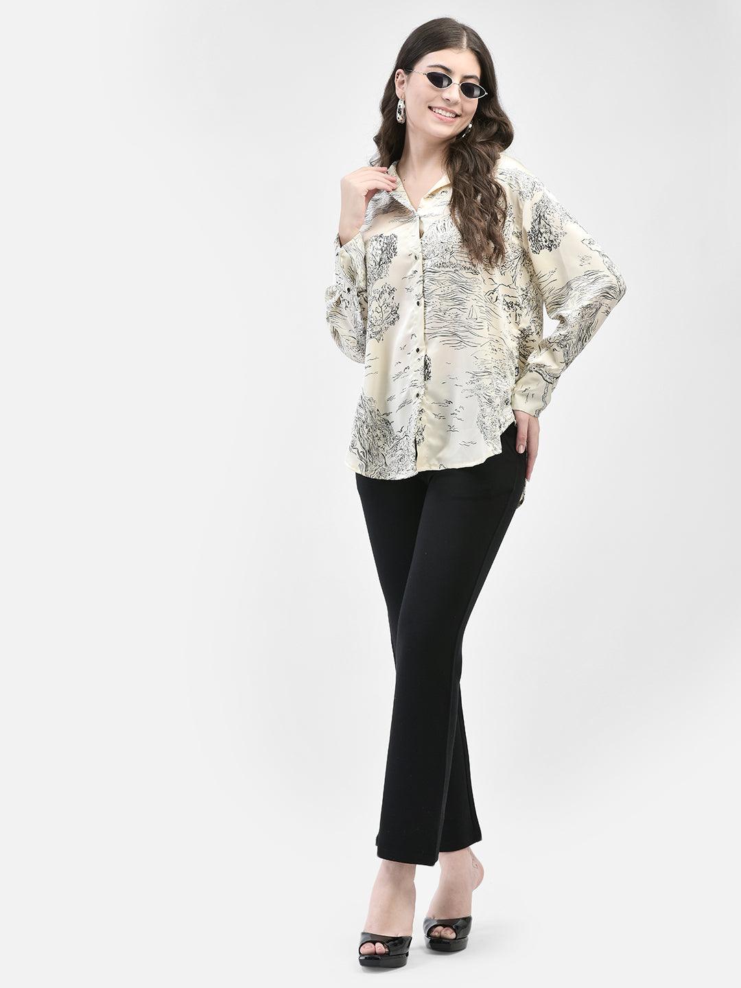 Full view of woman in beige satin print shirt and black pants, standing straight with neutral expression
